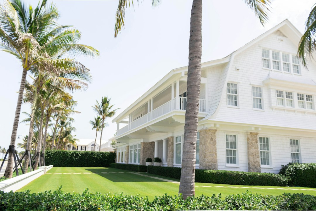 White coastal home with palm trees and a green lawn